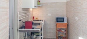 A compact kitchenette with a gas stove, sink, and a microwave on a small shelf.