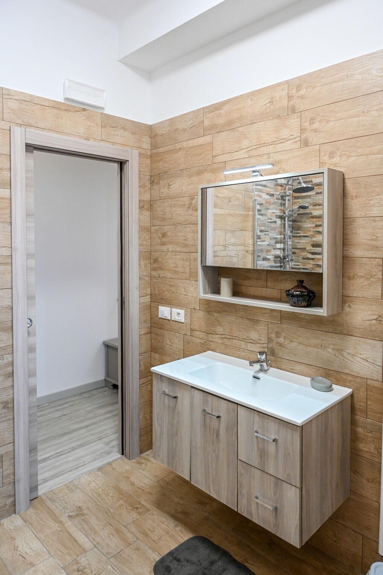 Une salle de bain moderne avec un meuble-lavabo en bois, une douche intégrée et un lavabo blanc.