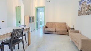A spacious living area with a beige sofa, a dining table with chairs, and a cabinet.