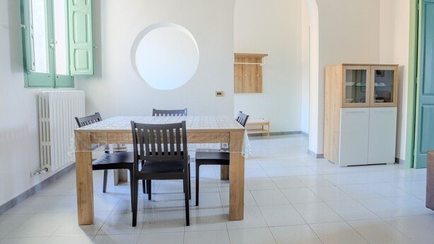 A dining area with a round table, chairs, a radiator, a cabinet, and an arched doorway.