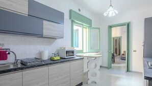 A modern kitchen with a built-in microwave, a sink, and a countertop. There is a window with green shutters and a pendant light above the counter.