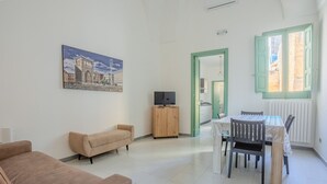 A living room with a sofa, a TV on a wooden cabinet, and a dining area with a table and chairs.
