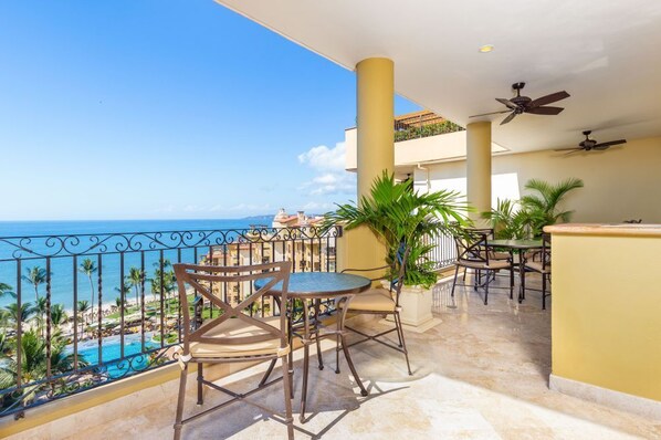 A balcony with a view of the ocean, featuring outdoor seating and ceiling fans.