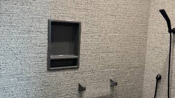 A small, enclosed shower area with a textured wall, a built-in shelf, and a handheld showerhead.
