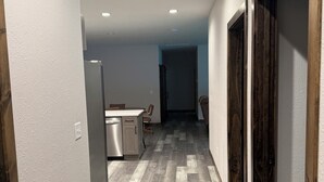 Un pasillo con espacio de cocina, piso de madera y una puerta a la derecha.