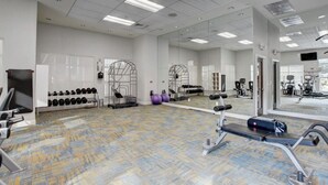 Une salle de sport équipée de matériel d’exercice, de miroirs et dotée d’un sol à motifs.