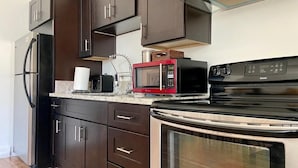 A kitchen with dark brown cabinets, a stainless steel refrigerator, a red microwave, and a black stove.