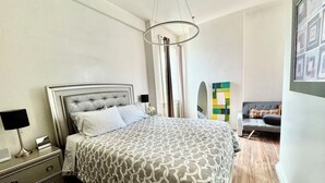 A modern bedroom with a tufted headboard bed, a bedside table with a lamp, and a colorful abstract painting on the wall.