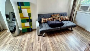 A modern living room with a grey sofa, patterned cushions, a colorful abstract painting, and a wooden floor.