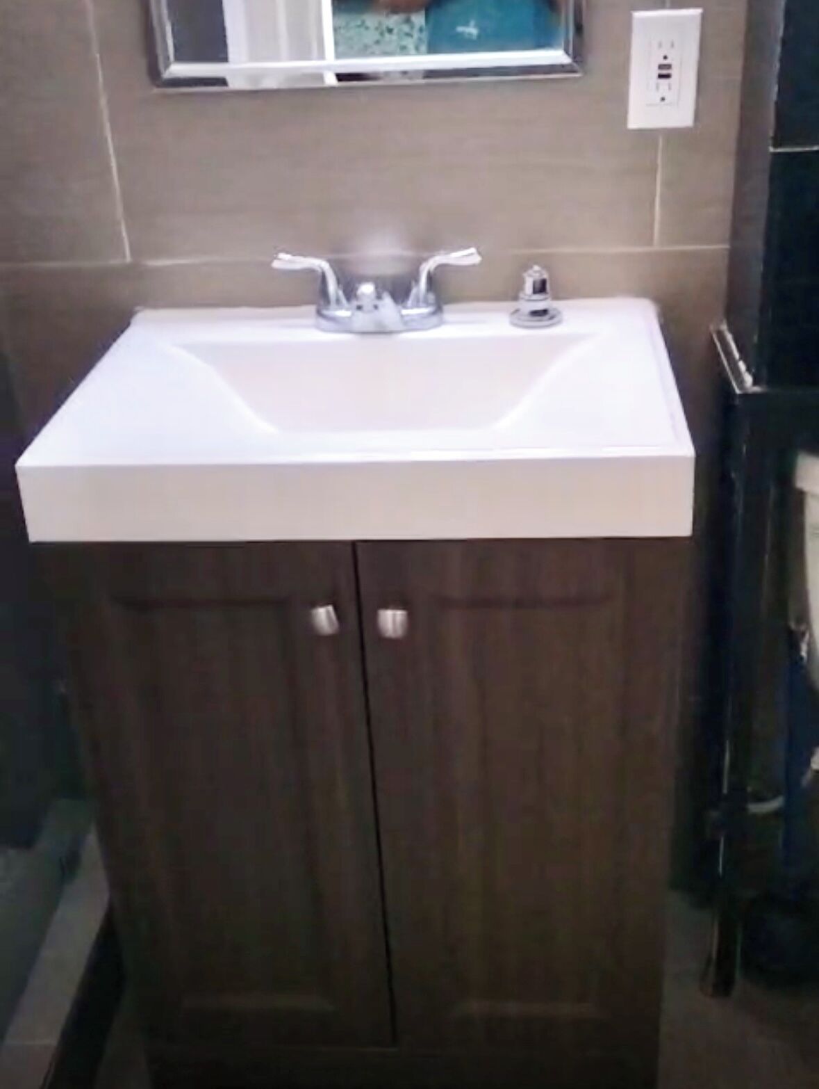 Ein Badezimmer mit einem weißen Waschbecken, Holzschränken und einem Spiegel darüber.