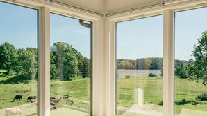 A room with large windows offering a view of a grassy field with cows and a lake. - Farm idyll with lake views, private beach spot & boat near the west coast (Västra Götalands län)