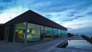 Et moderne hus med stor glasfacade, træterrasse og swimmingpool.