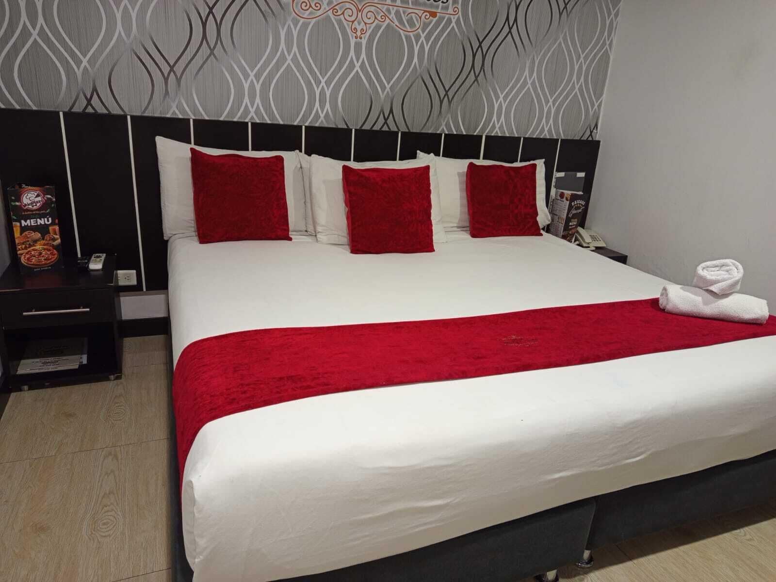 A large bed with white and red bedding, a red throw blanket, and a black headboard.