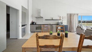 A modern kitchen with a dining area, featuring a large wooden table and chairs, a built-in oven, and a view of the outdoors. - Hurunui River Retreat - Tussock Cottage (Canterbury)
