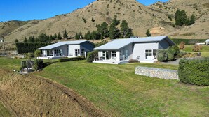 A modern two-story house with a large front lawn, surrounded by a hilly landscape. - Hurunui River Retreat - Tussock Cottage (Canterbury)