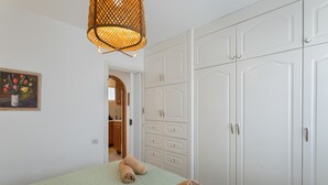 Ein Schlafzimmer mit Bett, Kleiderschrank, einem Gemälde und einer Pendelleuchte.