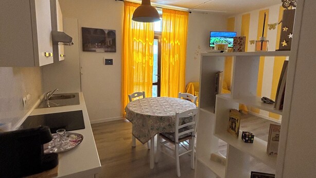 A compact kitchen with a dining area, a small TV, and a shelf with various items.