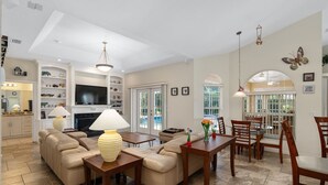 A spacious living room with a fireplace, a dining area with wooden chairs, and a kitchen with white cabinets. - Charming Golf Retreat - Pool/hot tub sleep 6 (Inverness)