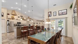 A modern kitchen with stainless steel appliances, a dining area with a glass table, and a large window providing natural light. - Charming Golf Retreat - Pool/hot tub sleep 6 (Inverness)