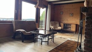 A cozy living room with a wooden floor, a glass coffee table, leather sofas, a fireplace, and a large window with a view. - Urlaubsstube1982 - wildly romantic with a fireplace and rustic charm (Schöfweg)