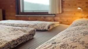 A room with two beds, wooden walls, and a window with curtains. - Urlaubsstube1982 - wildly romantic with a fireplace and rustic charm (Schöfweg)