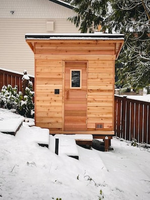 A wooden cabin with a door and window, surrounded by snow.