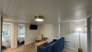 Una camera d'albergo moderna con un divano blu, una panca in legno, un tavolino, una TV fissata al muro e una lampada da terra.