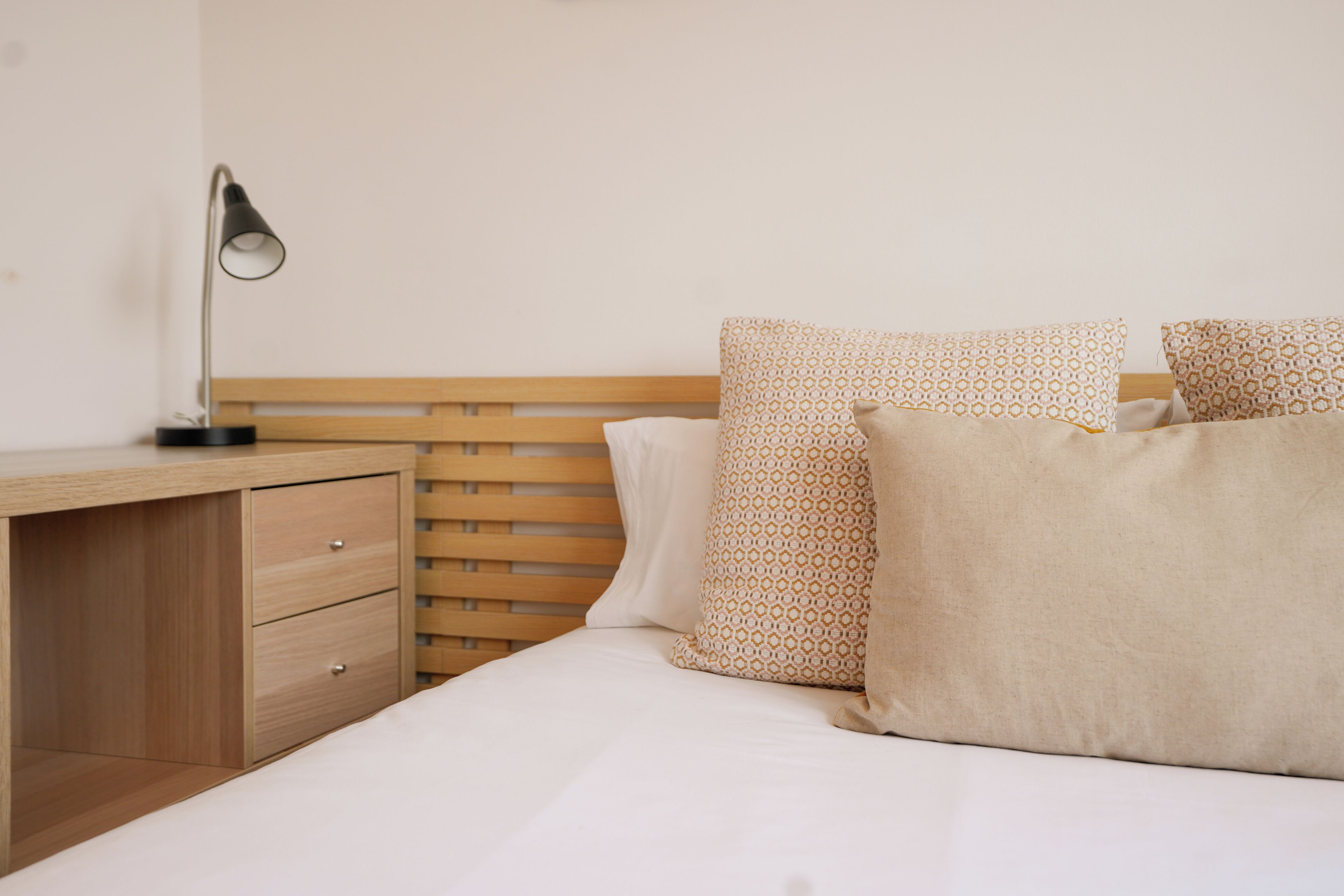 A neatly made bed with patterned pillows, a bedside table with a lamp, and a wooden headboard.