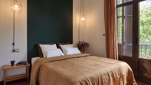 A bedroom with a large bed, two bedside lamps, a bedside table with books, and a window with shutters. - Stay U-nique Apartments Ronda Sant Pere (Barcelona)
