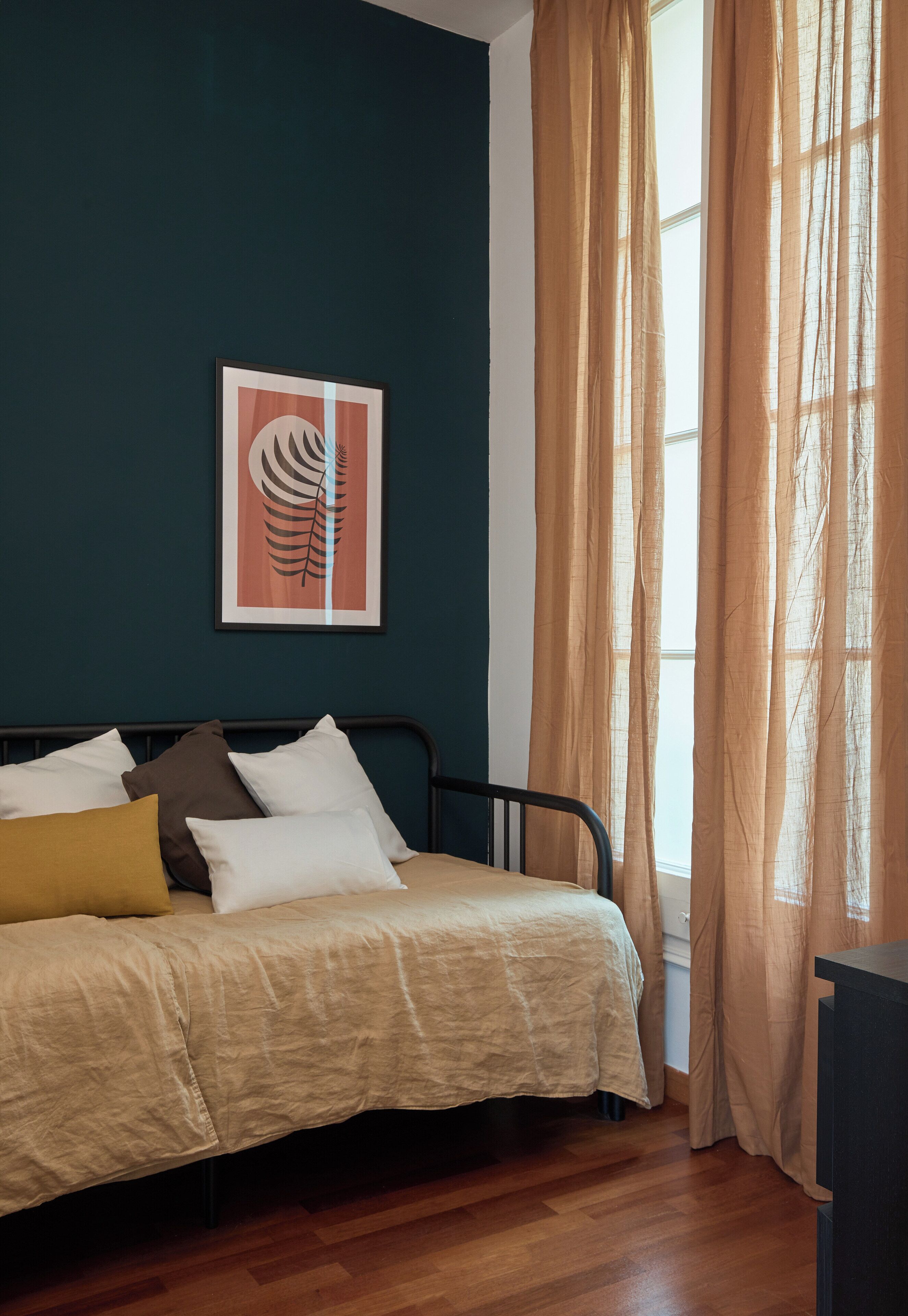A bedroom with a bed, a framed artwork on the wall, and a window with curtains.