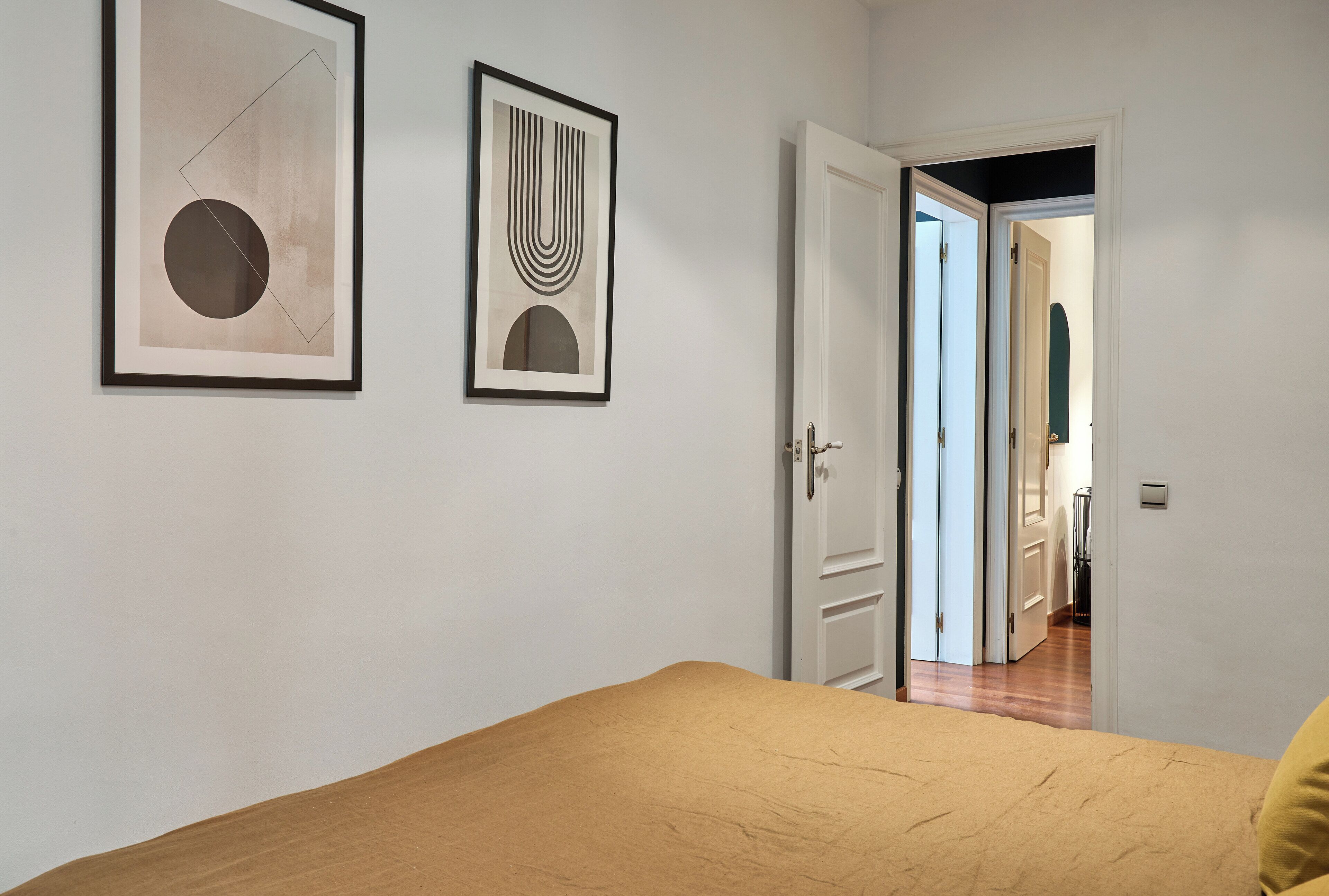 Une chambre à coucher avec un lit, deux œuvres d’art encadrées accrochées au mur et une porte donnant sur une autre pièce.