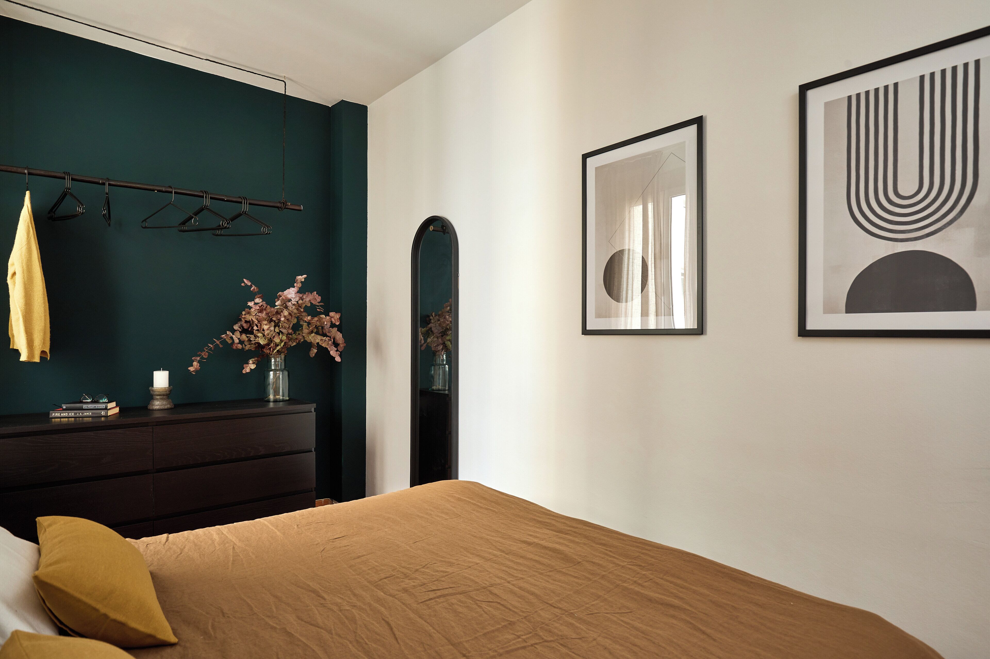 A bedroom with a bed, a dresser, a mirror, and wall art.
