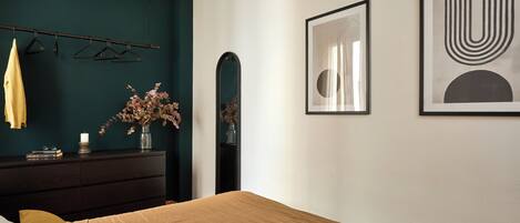 A bedroom with a bed, a dresser, a mirror, and wall art.