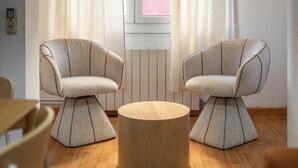 Zwei gepolsterte Sessel mit markantem Design, ein runder Holztisch und ein Holzboden.
