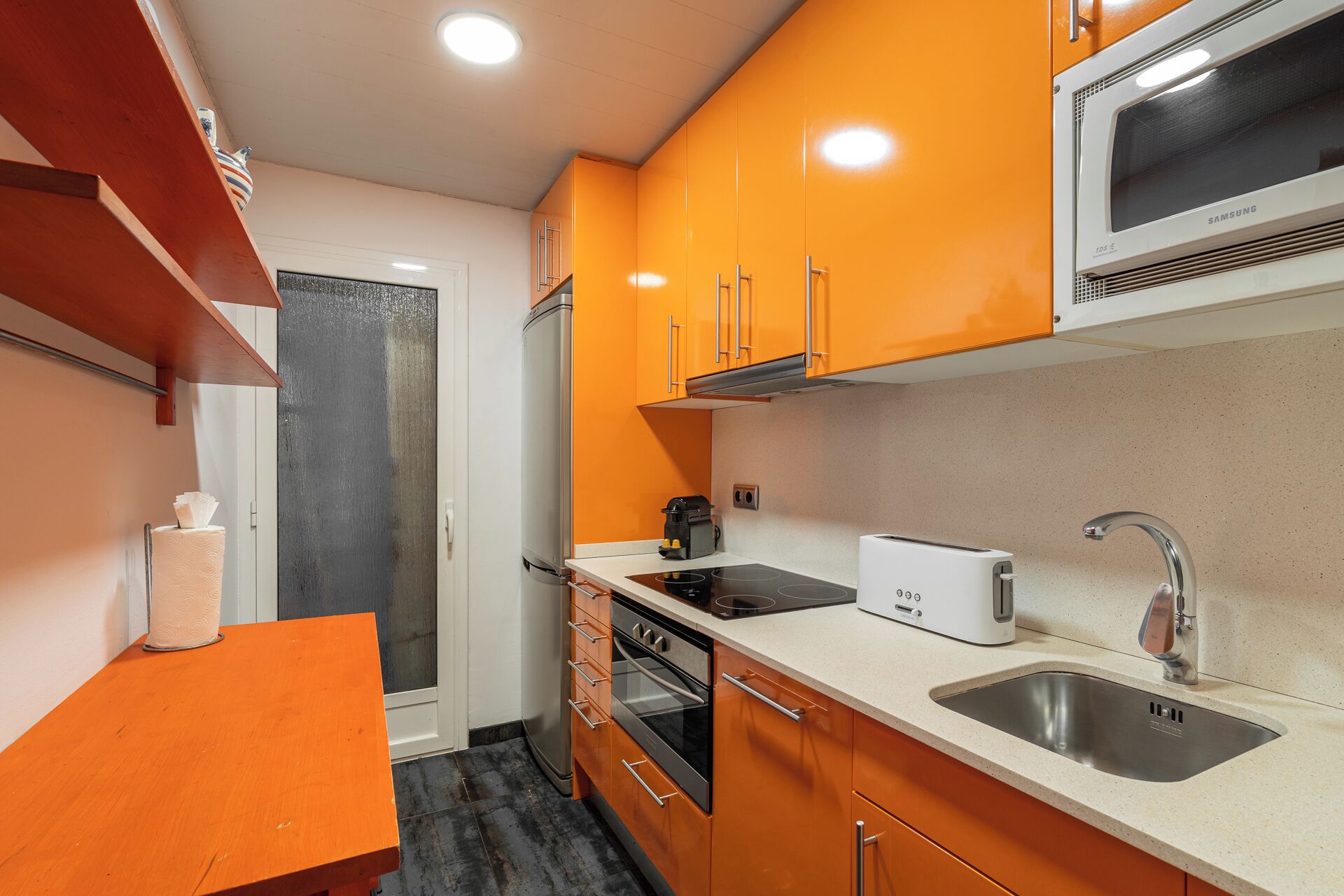 Une cuisine de taille réduite avec des meubles de couleur orange, un four à micro-ondes, un grille-pain et un évier.