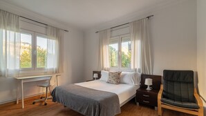 Ein Hotelzimmer mit Bett, Schreibtisch, Stuhl und zwei mit Vorhängen versehenen Fenstern.