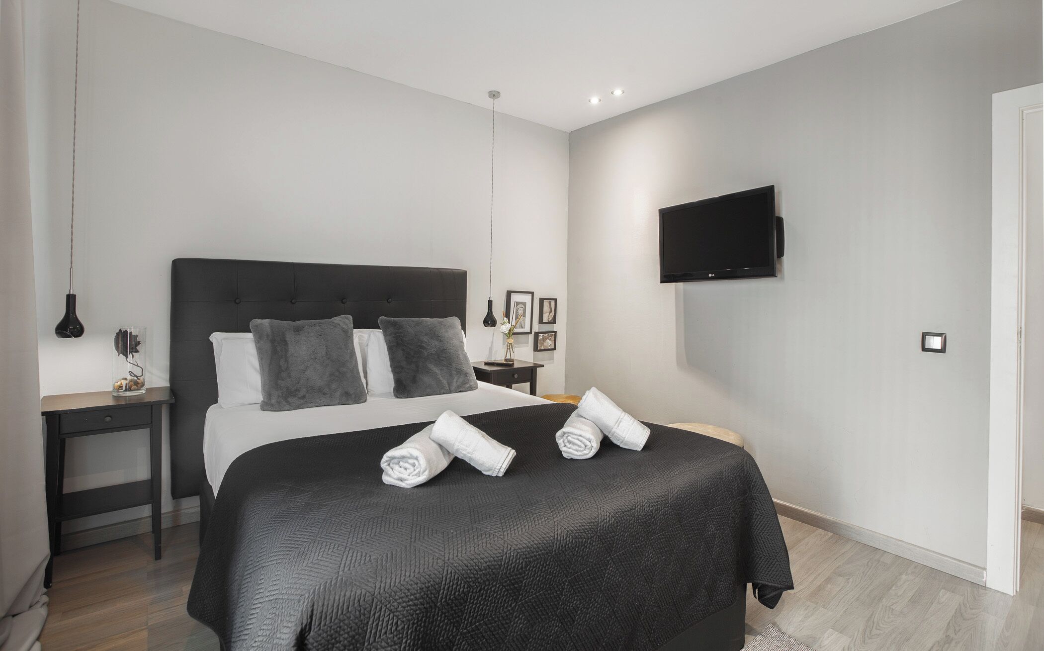 Quarto moderno com uma cama grande, televisão de tela plana na parede e mesa de cabeceira com abajur.