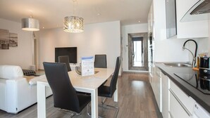A modern kitchen with white cabinets, a black countertop, and a stainless steel sink. There is a dining area with a white table and black chairs. - Stay U-nique Apartments Aprestadora (L'Hospitalet de Llobregat)