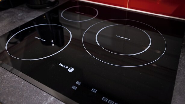 Une plaque de cuisson à induction noire, dotée de trois zones de cuisson circulaires et d’un panneau de commande à boutons.