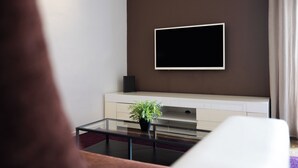 Un salon moderne avec un téléviseur à écran plat fixé à un mur marron, un meuble de rangement blanc en dessous, et une table basse en verre agrémentée d’une plante.
