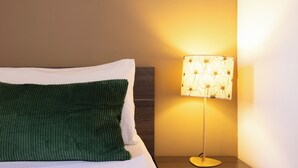 Un lit bien fait, avec un oreiller vert et une lampe de chevet à motifs floraux.