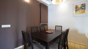 Un coin repas avec une table en bois foncé, six chaises, un luminaire et un tableau accroché au mur.