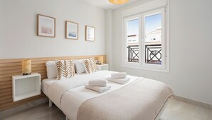 A bedroom with a bed, bedside tables, a window with a view, and framed pictures on the wall. - Stay U-nique Villa Mar Baltico (Benalmádena)