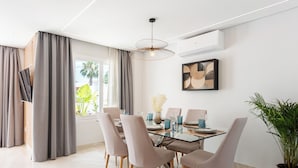 A modern dining area with a glass table, grey upholstered chairs, and a pendant light. - Stay U-nique Villa Mar Baltico (Benalmádena)