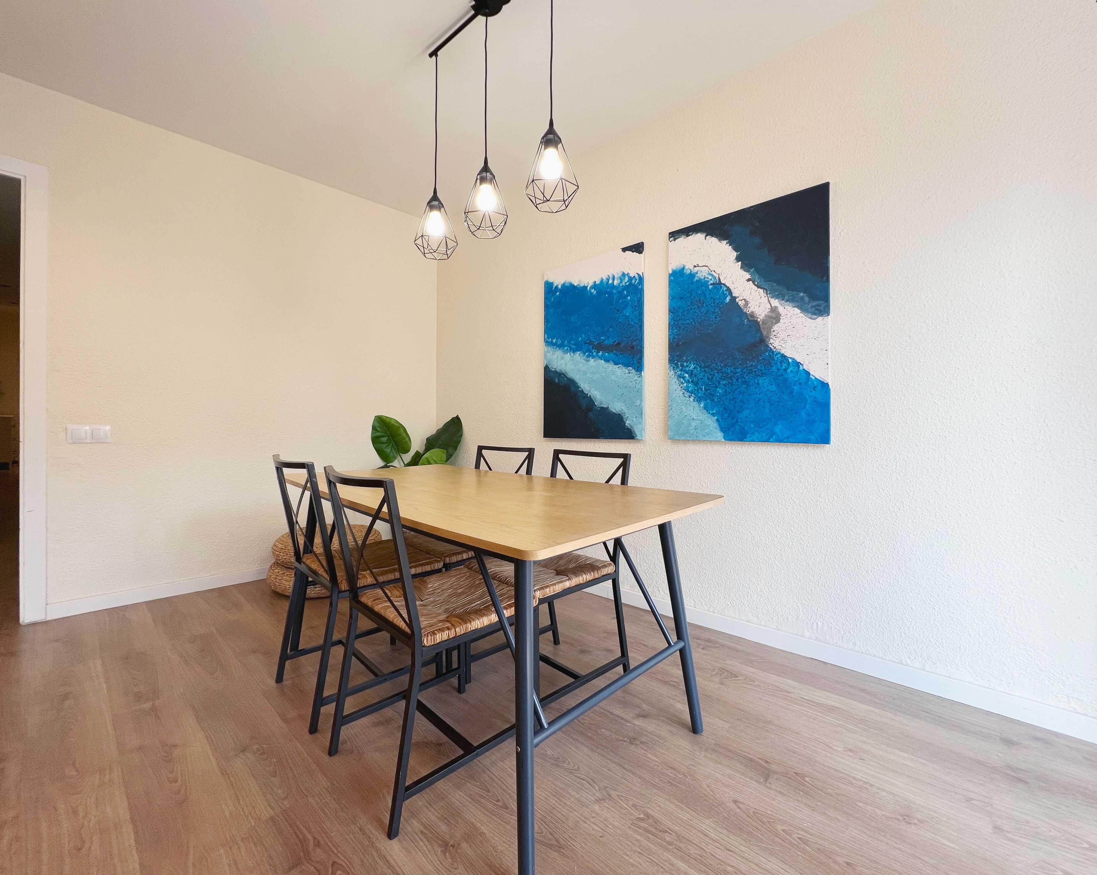 Un coin repas avec une table et des chaises en bois, un luminaire suspendu et deux tableaux abstraits accrochés au mur.
