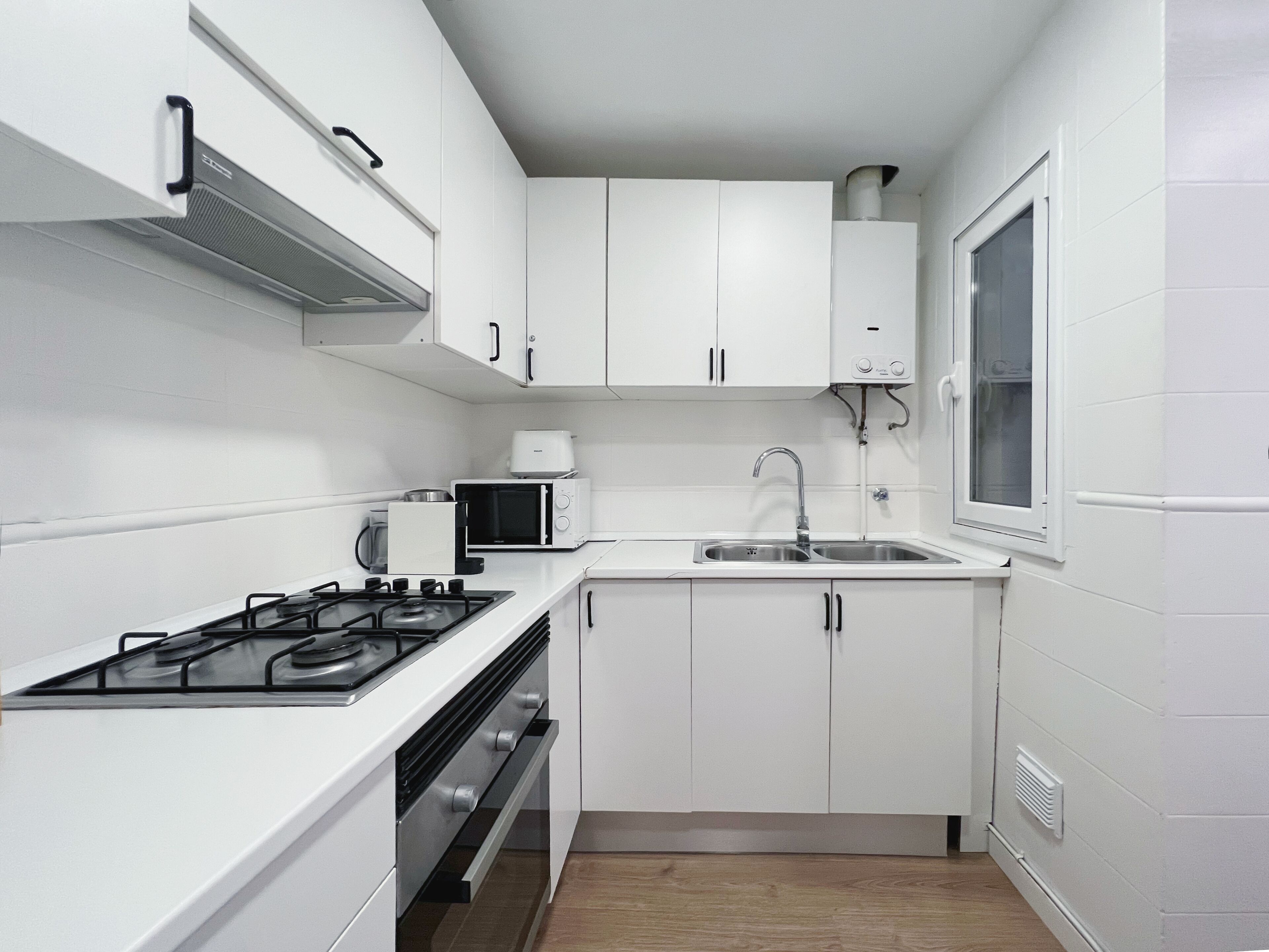 Una cocina compacta con armarios blancos, microondas, estufa y ventana.
