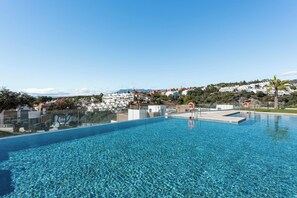 Une piscine d’un bleu éclatant, avec vue sur des bâtiments blancs et une montagne en arrière-plan.