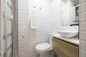 Un baño moderno con azulejos blancos tipo metro, un inodoro blanco, un tocador de madera y un espejo grande.