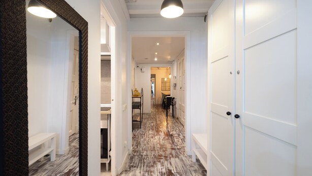 A hallway with white doors, a wooden floor, and a hanging light fixture.