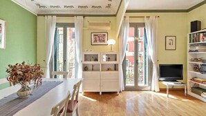 Una sala de estar con una mesa de comedor, armarios blancos, un televisor y una estantería.